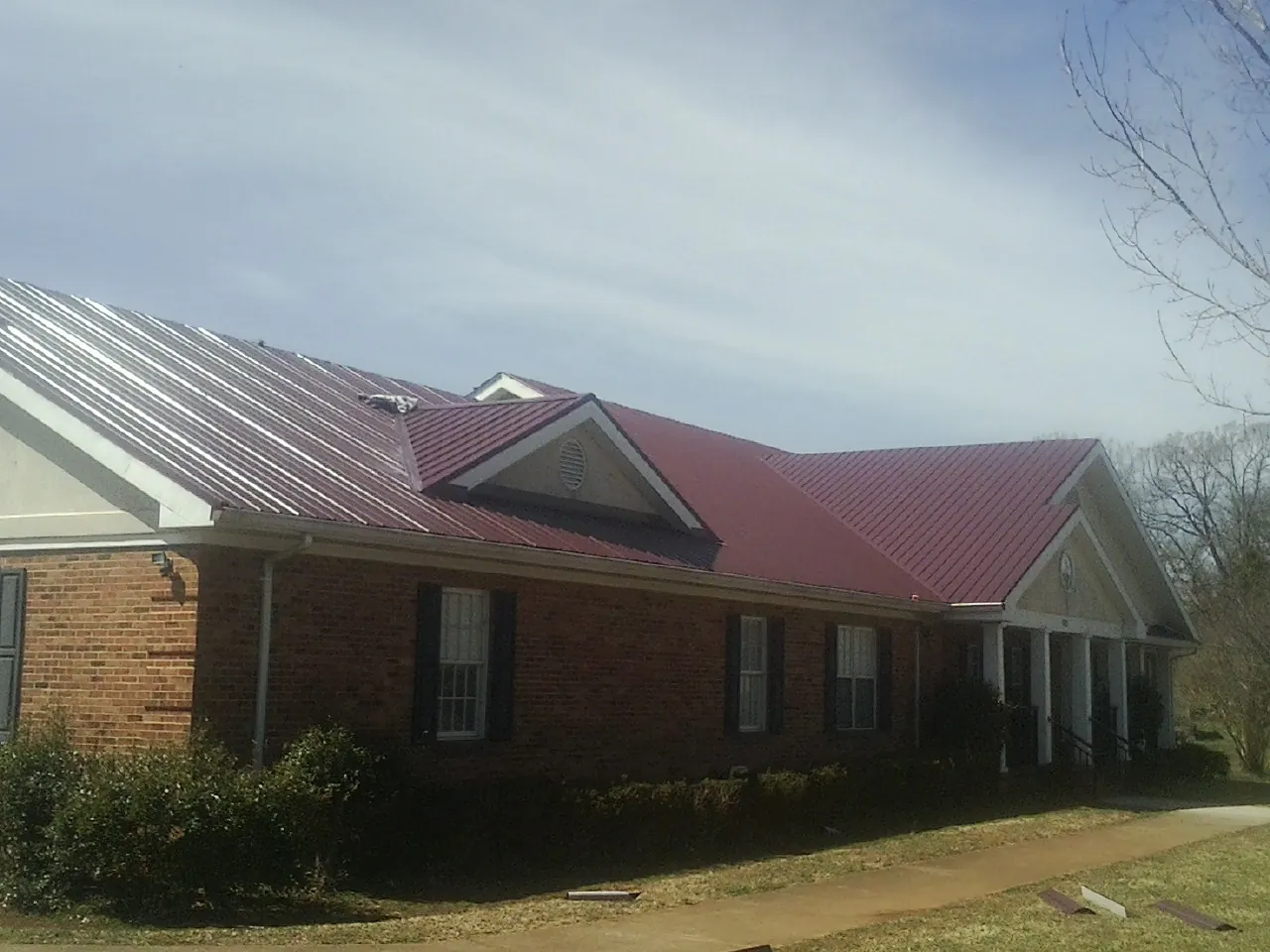 Red metal roof with gabled entries on a long brick building, from a Hail Damage Roof Repair job in Huguenot