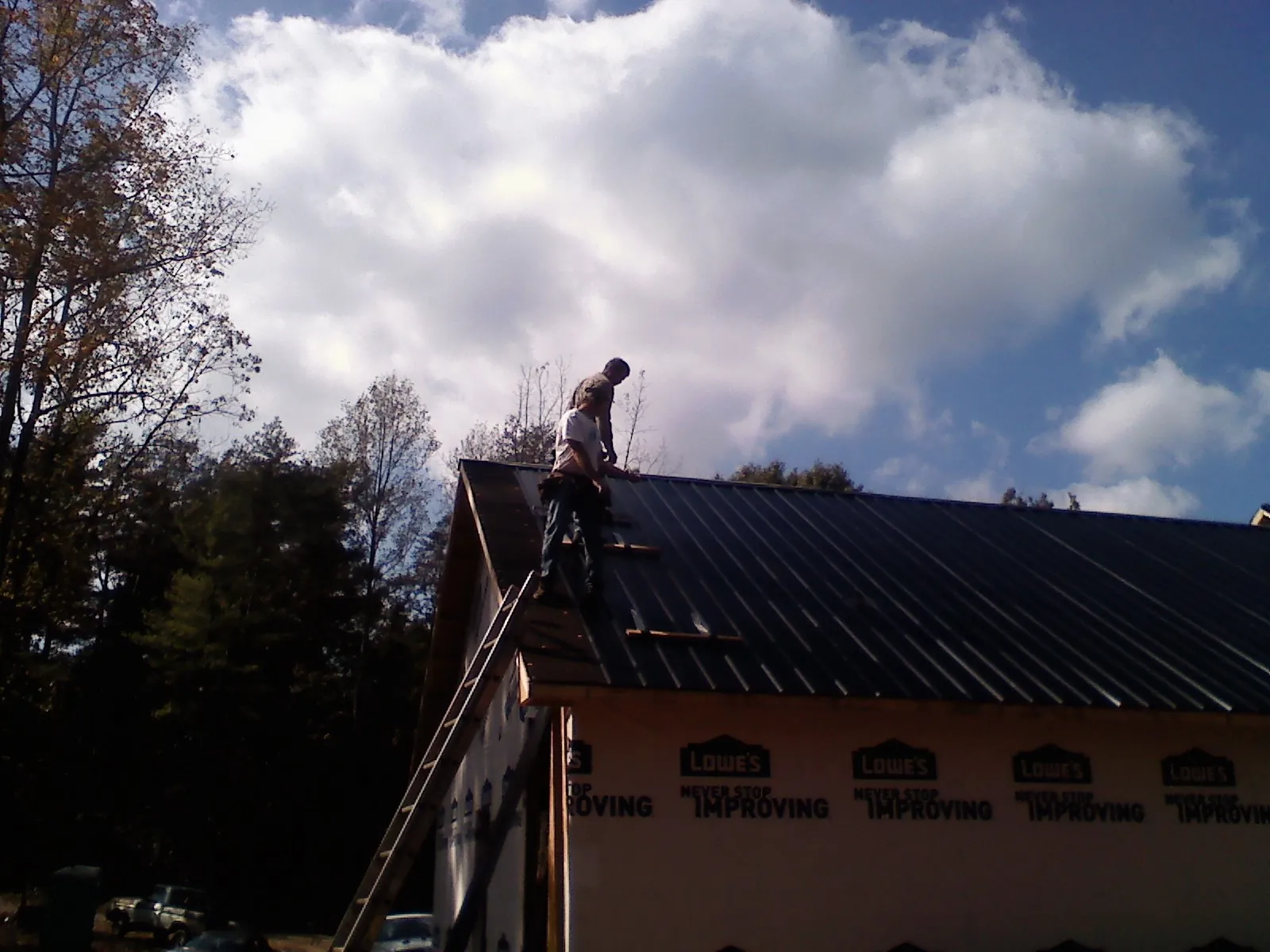 Roofer fastening dark metal panels high against a cloudy sky, from a Roof Inspection job in Huguenot