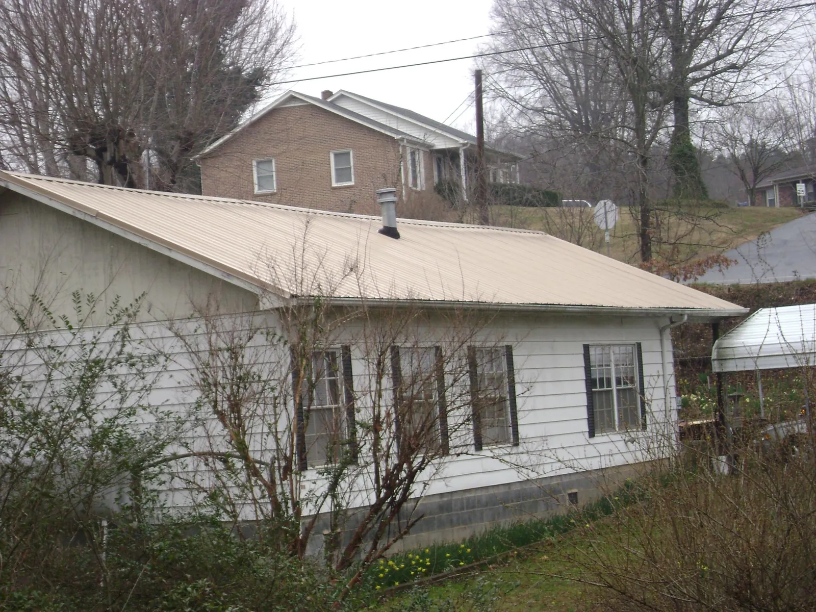 Tan metal roof on a white sided house set into a hillside — Commercial Roofing by Roofing Brothers in Huguenot