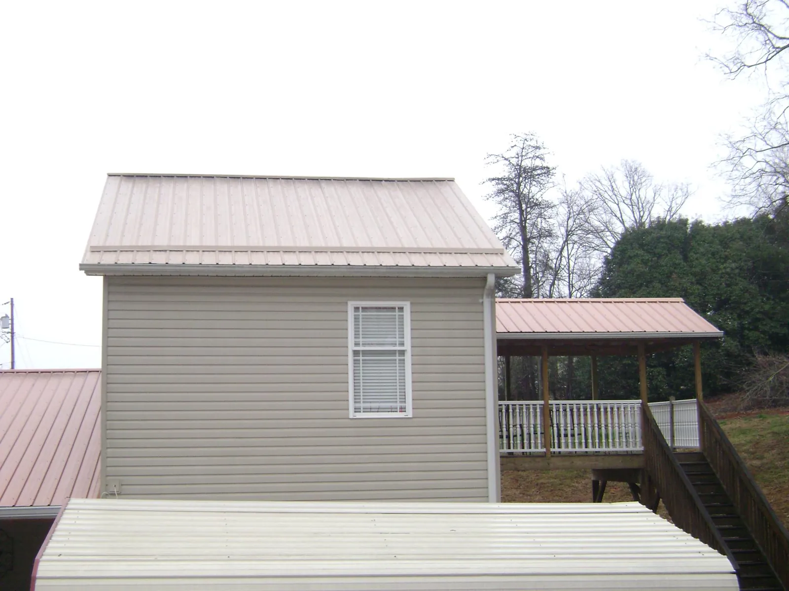 Tan metal roofs on a two story addition and attached porch, from a Roof Replacement job in Huguenot